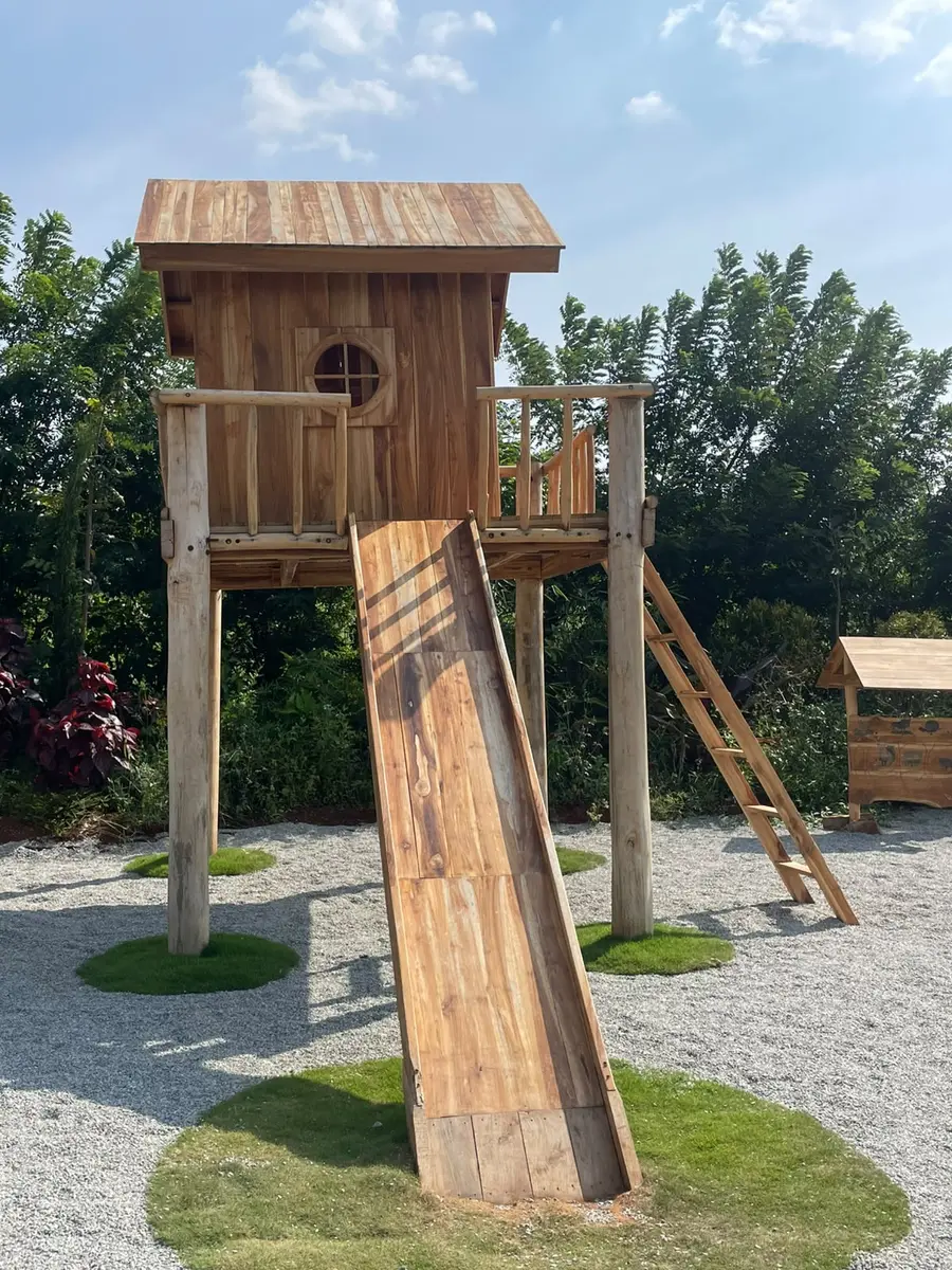 A timber treehouse with a long wooden slide and a ladder, on gravel and lawn